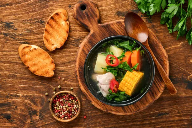 Photo of Chilean meat soup with pampkin, corn, fresh coriander and potatoes on old wooden table background. Cazuela. Latinamerican food.