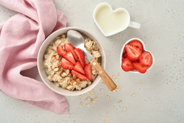 porridge di farina d'avena con fette di fragola, mandorle di noci e miele in ciotola blu su tavolo grigio. alimentazione sana, dieta, concetto di cibo vegetariano. posizione per il testo - oatmeal heat bowl breakfast foto e immagini stock