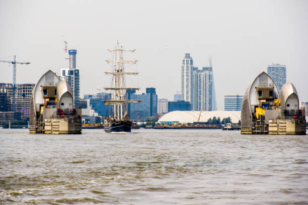 A tall ship passing throughthe gate formed by the Thames Barrier, during the tall ship Festival in Greenwich, the Greater London, UK. This retractable barrier system were created to serve as a Flood defence, protecting most of Greater London from being flooded by exceptionally high tides and storm surges from the North Sea