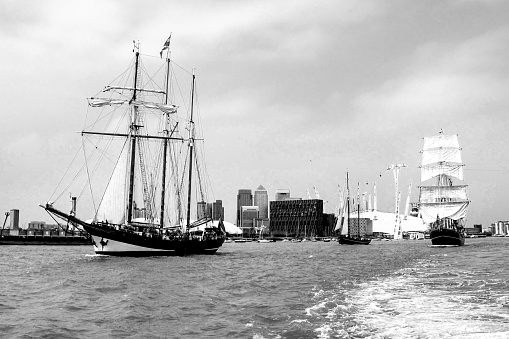 Two different types of sailing ships, in black and white,  on the river Tames, sailing out towards the ocean, with the Buildings of Canary Wharf, greater London, UK, in the background. Photographed during the Tall ship festival of 2014. These are examples of a schooner and a barque,