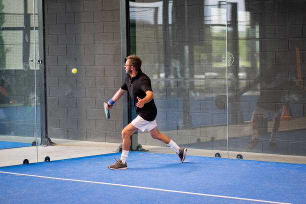 hombre jugando al pádel en una pista de pádel de hierba azul bajo techo - joven deportista que golpea la pelota con una raqueta - tennis in a row team ball fotografías e imágenes de stock