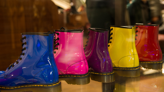 Five shining boots in a row in a storefront. Same model, five different colours: blue, pink, lila, yellow and red. London, UK, Europe