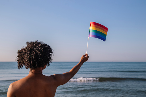 Young man with afro hair raises a pennant with lgtbi colors