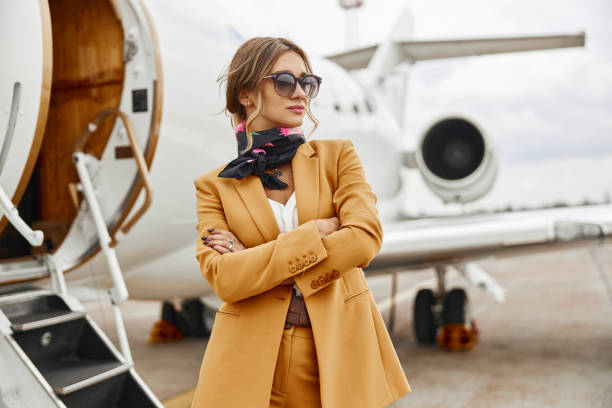 Businesswoman with crossed arms near airplane jet Businesswoman stand near airplane jet. Modern private plane with ladder. Young woman with crossed arms wear formal suit and glasses. Civil commercial aviation. Concept of air travel and business military private stock pictures, royalty-free photos & images