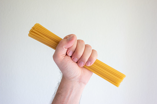Caucasian male hand holding a stack of raw long spaghetti close up shot isolated on white