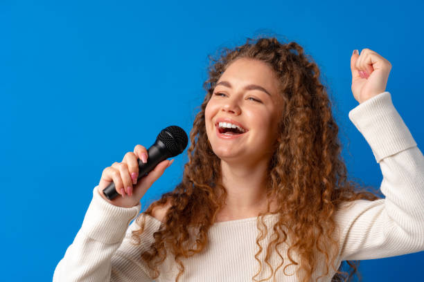 istock Young joyful curly-haired woman singing in microphone against blue background 1329902015
