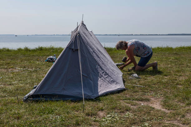 istock woman setting up a tent at the waterline 1329902132