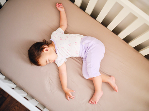 An 18 month old baby girl, asleep in a crib.