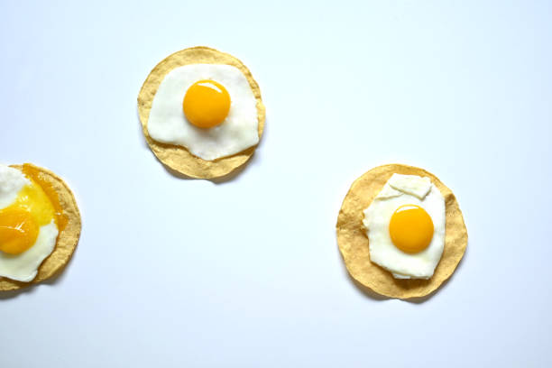 Overhead photograph of fried eggs with tortilla and broken egg