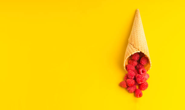 istock Raspberry explosion in a waffle cone on a yellow table. View from above. Healthy food concept. Minimalism. Copy space. 1329909853