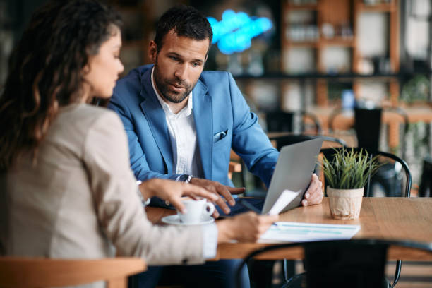 istock Young entrepreneur using laptop while going through business reports with colleague in a cafe, 1329913148