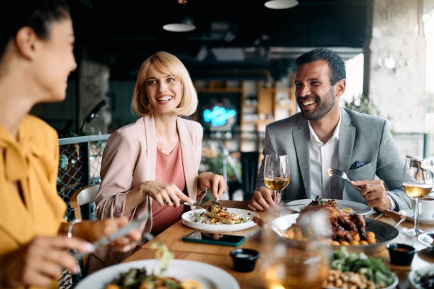 Happy business colleagues talking while eating lunch in a restaurant. Group of happy entrepreneurs communicating while enjoying in business lunch in a restaurant. business dinner stock pictures, royalty-free photos & images