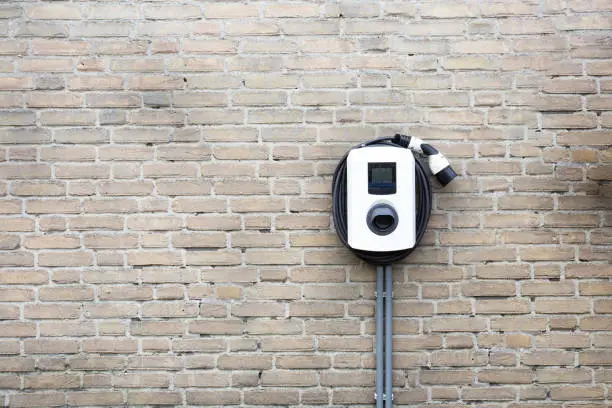 Photo of New charging station for electric car on brick wall at home, charging pillar with copy space ,