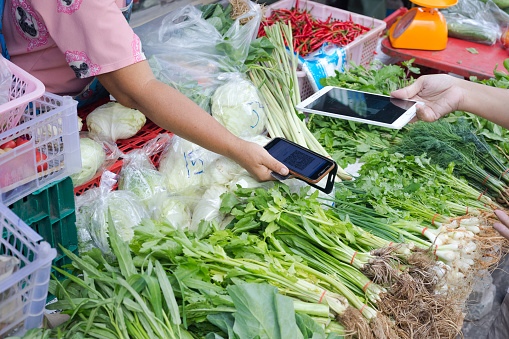 Thai woman is purchasing by contactless payment on local market in Bangkok. Both vendor and customer are holding mobiles for QR code scanning