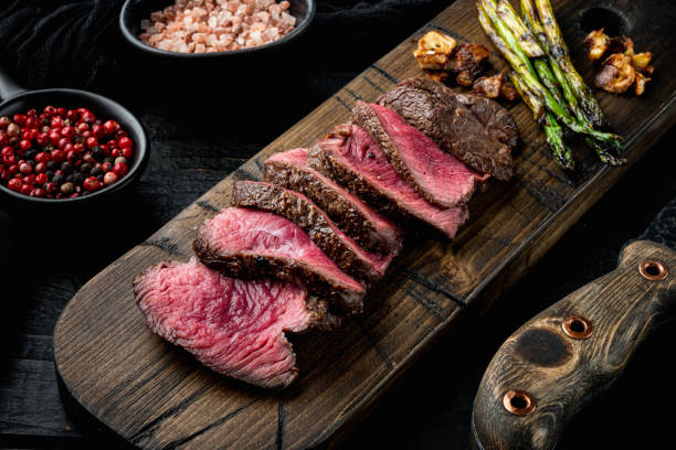 Grilled fillet beef steaks, with onion and asparagus, on wooden serving board, with meat knife and fork, on black wooden table background Grilled fillet beef steaks set, with onion and asparagus, on wooden serving board, with meat knife and fork, on black wooden table background scaloppini stock pictures, royalty-free photos & images