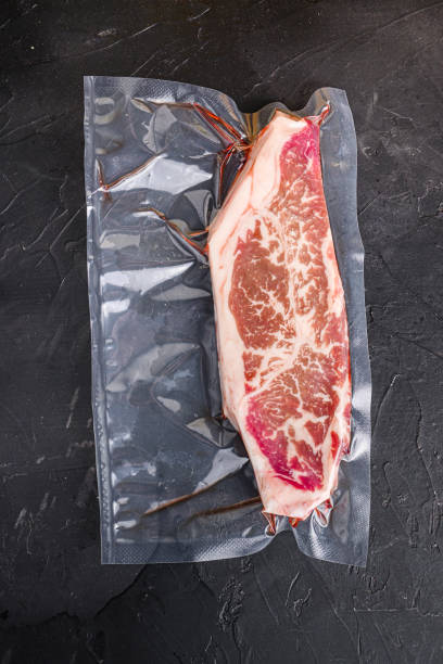 istock Vacuum packed organic beef  top blade steak for sous vide cooking  on black textured background, top view. 1329922819