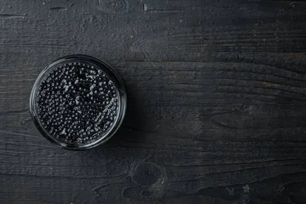 Black Caviar jar, on black wooden table background, top view flat lay with copy space for text