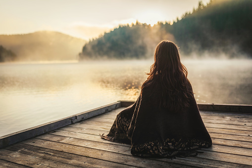 Woman relaxing / meditating near a lake in the morning.