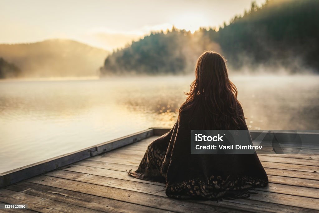 Woman relaxing in the nature Woman relaxing / meditating near a lake in the morning. Meditating Stock Photo