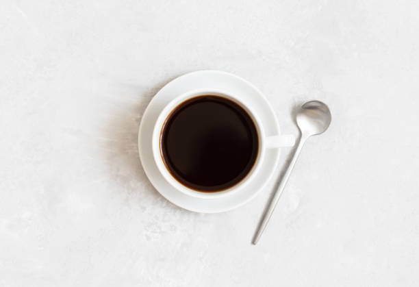istock Black coffee in a cup and silver spoon on a white concrete background. Top view, flat lay. 1329924092