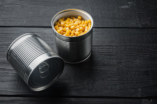 Lot of pieces of canned yellow corn, on black wooden table background with copy space for text