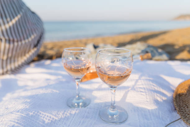 日没時のビーチでの夏のピクニック。ローズワインのグラスを持つ若い女性。週末のピクニック。クローズアップ。 - toast glass wine dinner ストックフォトと画像