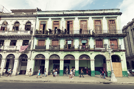 Cubans walking on the sidewalk in front of buildings in disrepair