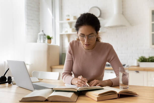 Concentrated young woman in eyewear reading educational book.