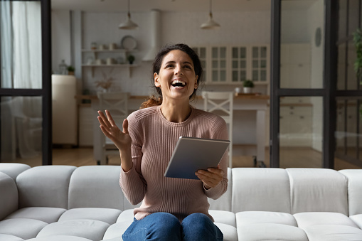 Sincere happy young hispanic woman celebrating internet success or giveaway lottery win, holding digital touchpad in hands. Overjoyed latin lady feeling excited of getting unbelievable online news.