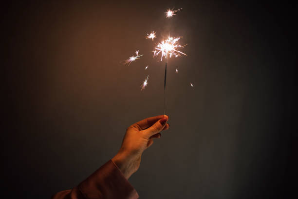 A New Year's sprinkler held by an unrecognizable woman's hand against a gray background