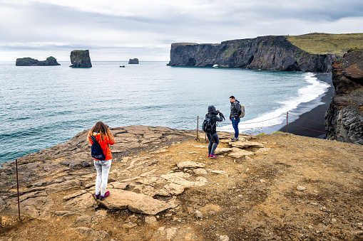 Myrdal, Iceland - June 14, 2018: Reynisfjara black sand beach and people tourists taking pictures with volcanic rocky cliff formations with seashore coastline in summer