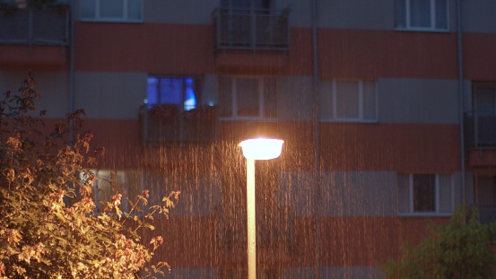Night rainy weather. The lighting lantern shines at night. Raindrops falling, splashing. Natural phenomenon of rainfall, lightning light reflection. Shaking the camera.