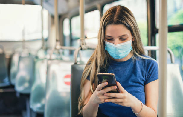 istock Student girl using smart phone while sitting in a bus. She's wearing a protective face mask to protect from coronavirus COVID-19. Back to school concept 1329932017