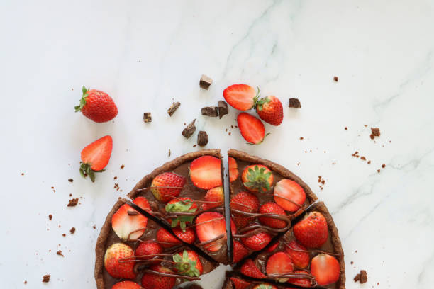 image de tranchées, tarte à la fraise au chocolat, croustillantes, cannelées, en croûte de cacao, garnies de fraises entières et coupées en deux arrosées de chocolat fondu, entourées de fraises et de morceaux de chocolat, fond d’effet marbre, vue - tart dessert chocolate fruit photos et images de collection