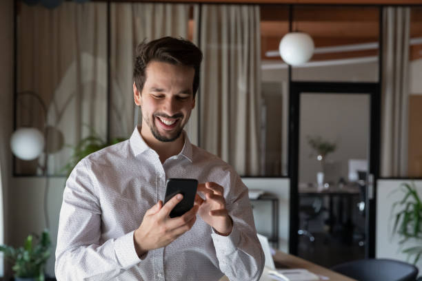 istock Head shot smiling businessman using smartphone standing in office room 1329936137