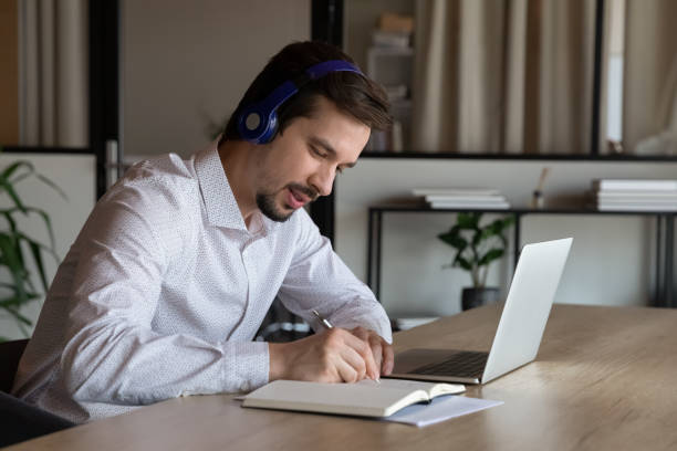 istock Employee in headphones taking notes, watching webinar in office 1329936152
