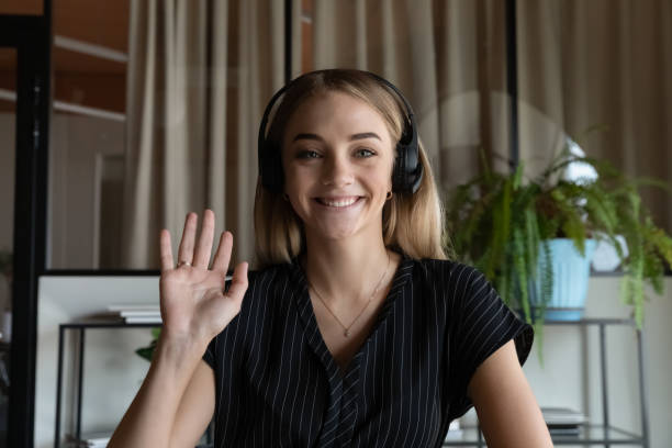 head shot portrait of smiling woman in headphones waving hand - gesprek coaching detail stockfoto's en -beelden