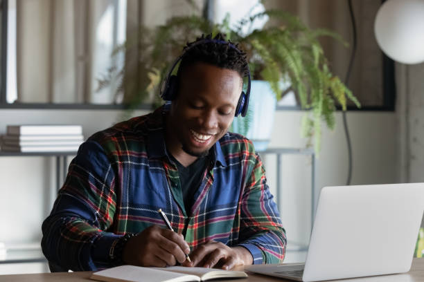 istock Smiling African American man in headphones taking notes, studying online 1329936187