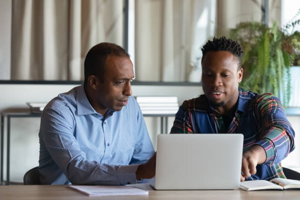 dos empleados afroamericanos trabajando en proyectos juntos, usando una computadora portátil - education business people men fotografías e imágenes de stock