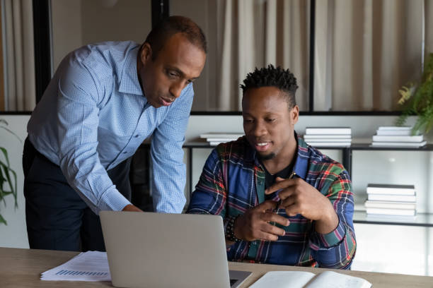 istock African American mentor teaching intern, pointing at laptop screen 1329936198