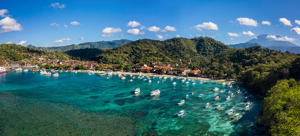 Aerial drone panorama taken by drone of the peaceful village of Padangbai located on the Eastern shore of Bali with the harbour being the main departure access to Lombok in Indonesia.