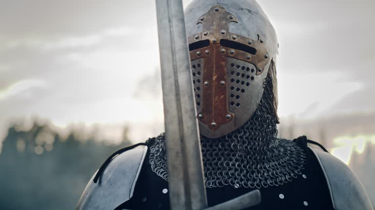 Medieval Knight Wearing Armour and Helmet, Draws Sword from Shearh, Ready to Fight, Kill His Enemy in Battle. Warrior Soldier on Battlefield. War, Invasion, Crusade. Cinematic Historic Reenactment