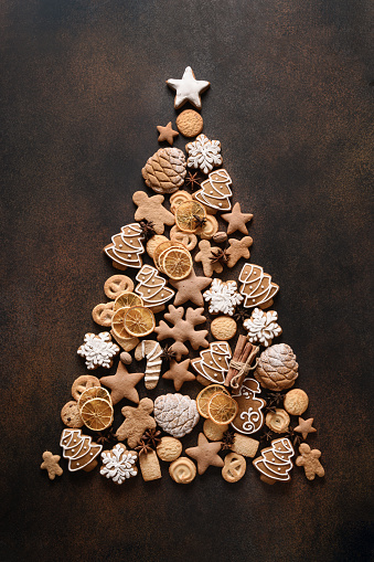Creative Christmas tree of assorted cookies, cinnamon, anise stars, berries, orange chips, on brown background. New Year greeting card. Top view. Xmas holiday background. Copy space.