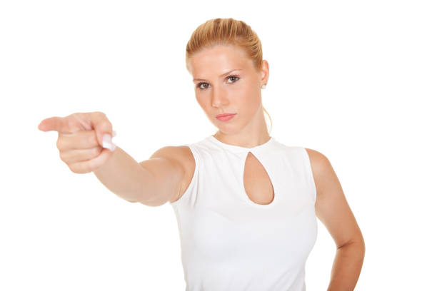 Portrait of a beautiful young woman pointing with her finger at the camera and laughing while standing in front of a bright blue background.