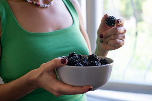 The woman holding and eating a bowl of freshly picked blackberries.