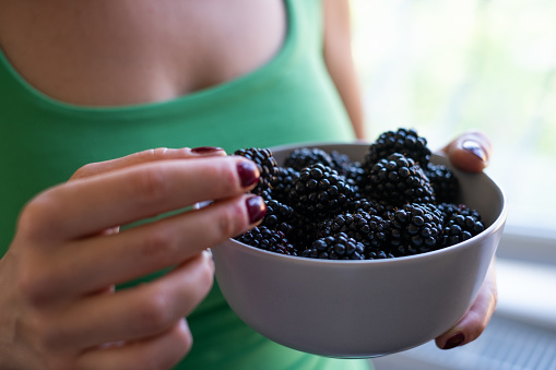 The woman holding and eating a bowl of freshly picked blackberries.
