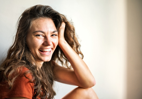 Portrait of cheerful woman sitting down with hand on head and looking at camera