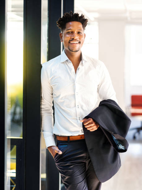 istock Young business man smiling while leaning against a wall in an office 1329949308