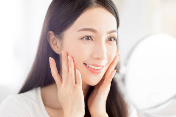 istock Beautiful Young woman  touching face skin and looking in mirror 1329952416