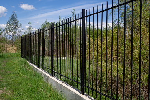 Long black transparent metal fence with concrete foundation against blue sky. Diagonal arrangement.